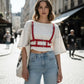 Adjustable cage chest harness with red faux-leather straps worn over a white cropped top