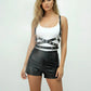 Black cross-strap grommet body harness with vegan leather straps and metal hardware over a white tank top.