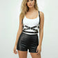 Black cross-strap grommet body harness in vegan leather with silver hardware worn over a white tank top.