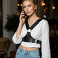 Black studded vegan leather chest harness with metal ring and studs worn over a white top.