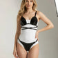 Two-piece black studded vegan-leather bralette and brief set with harness straps over a white base.