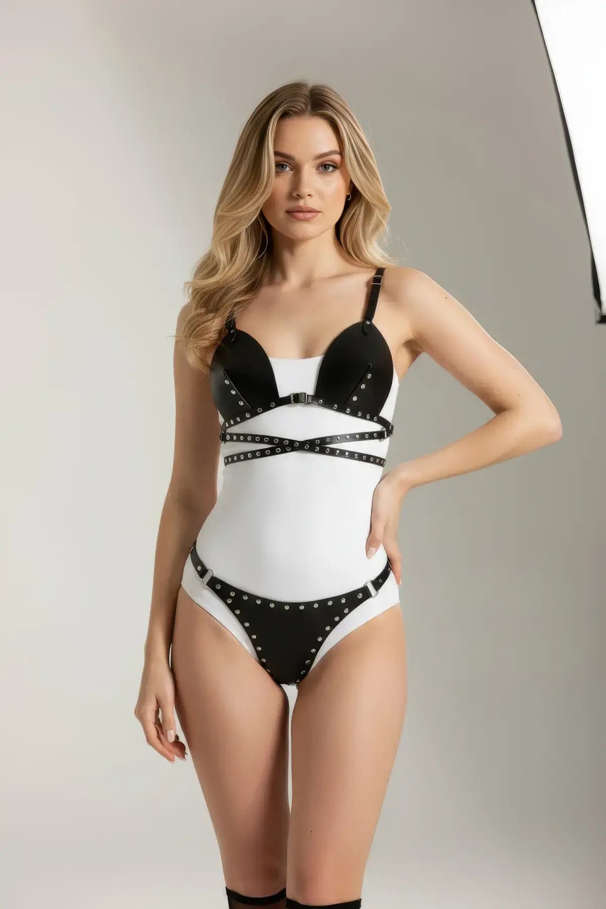 Two-piece black studded vegan-leather bralette and brief set with harness straps over a white base.