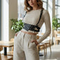 Black studded waist-panel harness in vegan leather worn over a cream ribbed top