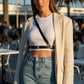 Black vegan leather cross-body harness belt worn over a white cropped top and blazer