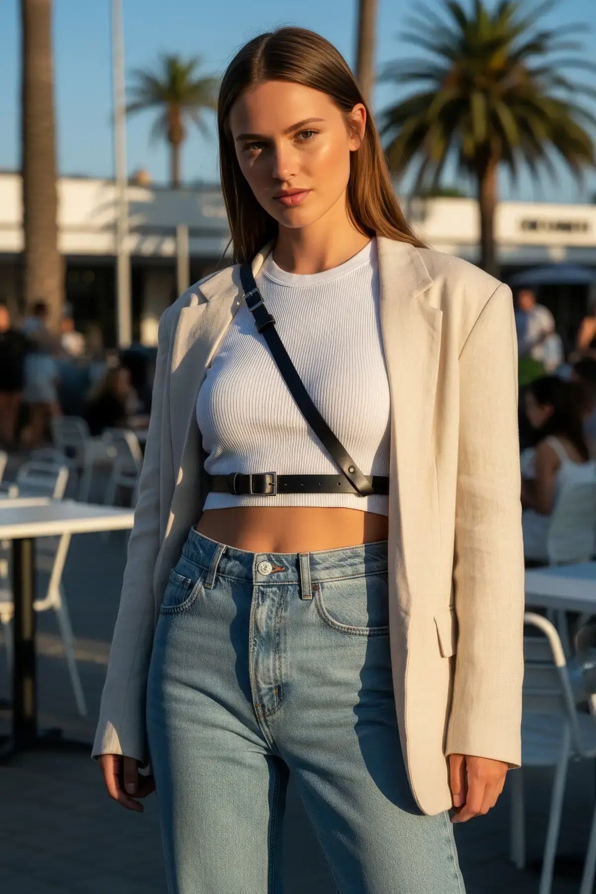 Black vegan leather cross-body harness belt worn over a white cropped top and blazer