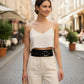 HarnessClub black wide O-ring vegan leather festival belt worn with white crop top and beige trousers.