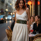 HarnessClub olive wide O-ring vegan leather belt on a model wearing a white dress at a stylish city cafe.