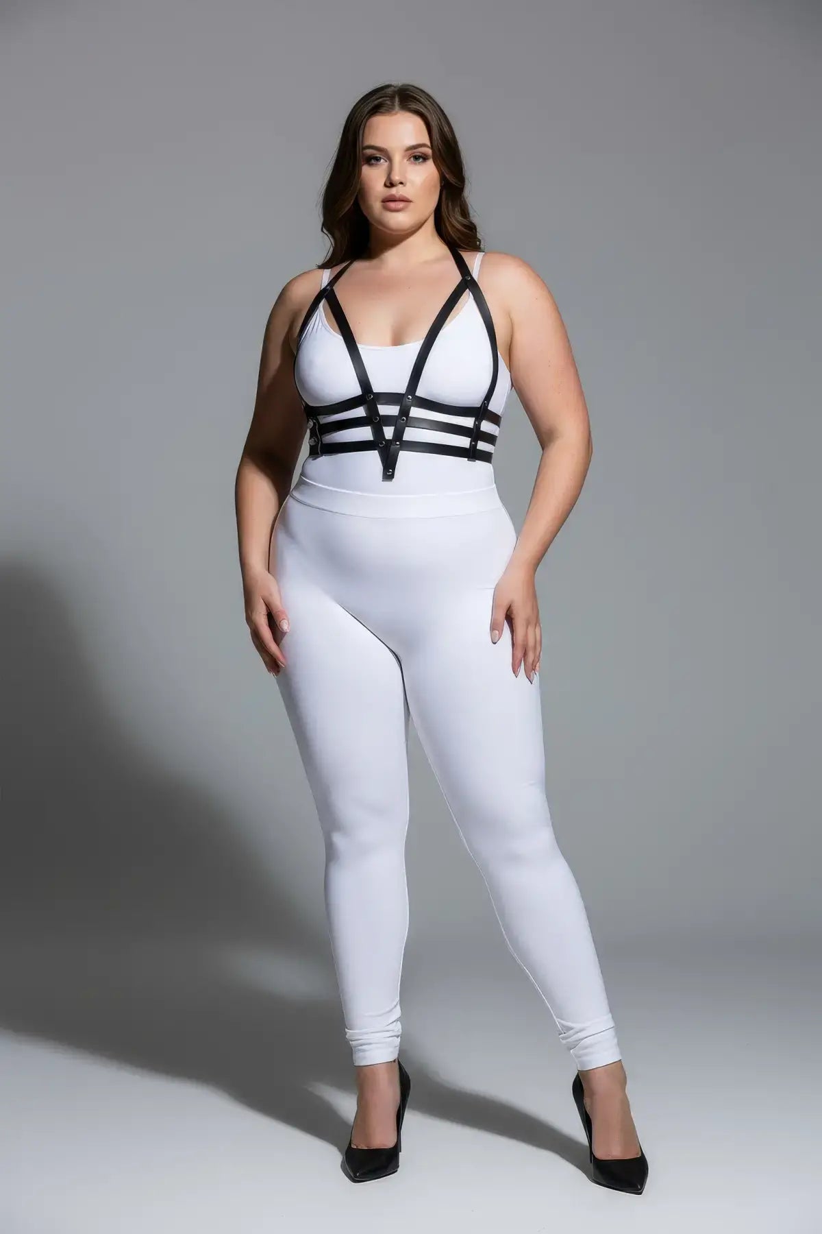 Plus size black adjustable faux-leather body harness by HarnessClub, worn over a white bodysuit