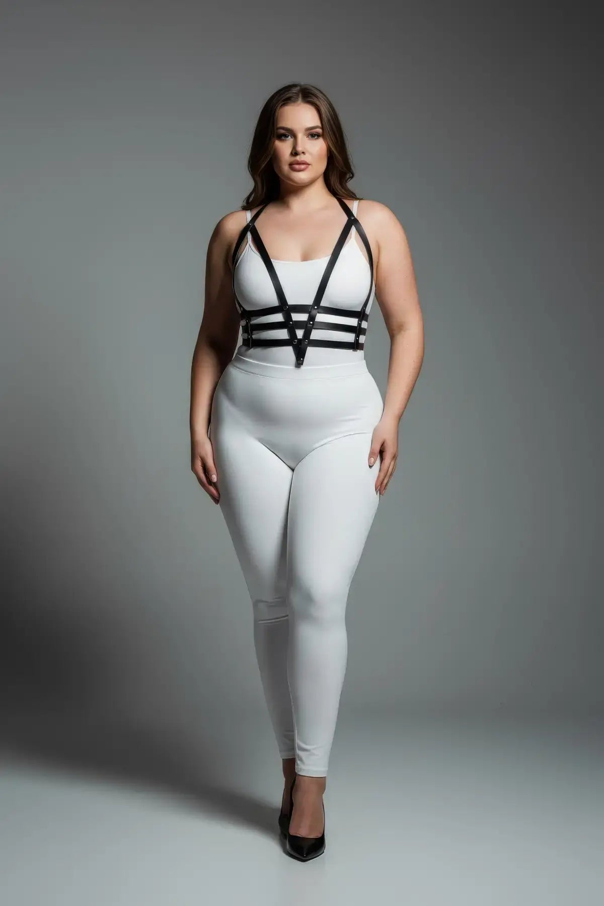 Plus size black adjustable faux leather body harness by HarnessClub worn over a white bodysuit.