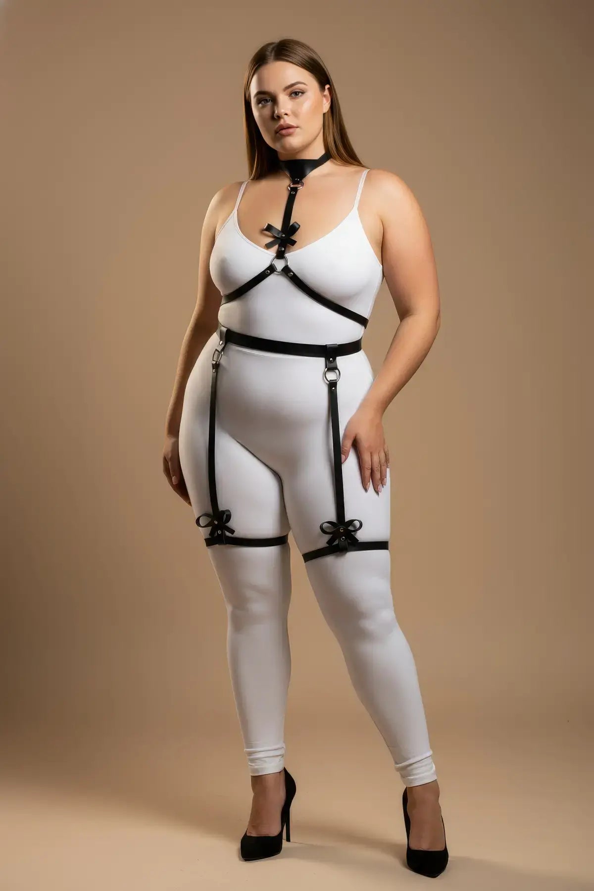 Plus Size Black Bow-Detail Faux Leather Garter Harness by HarnessClub on model; white bodysuit with leg straps.