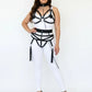 Plus Size black vegan leather body harness set with chain-back, worn over a white bodysuit; features metal rings and tassel fringe.
