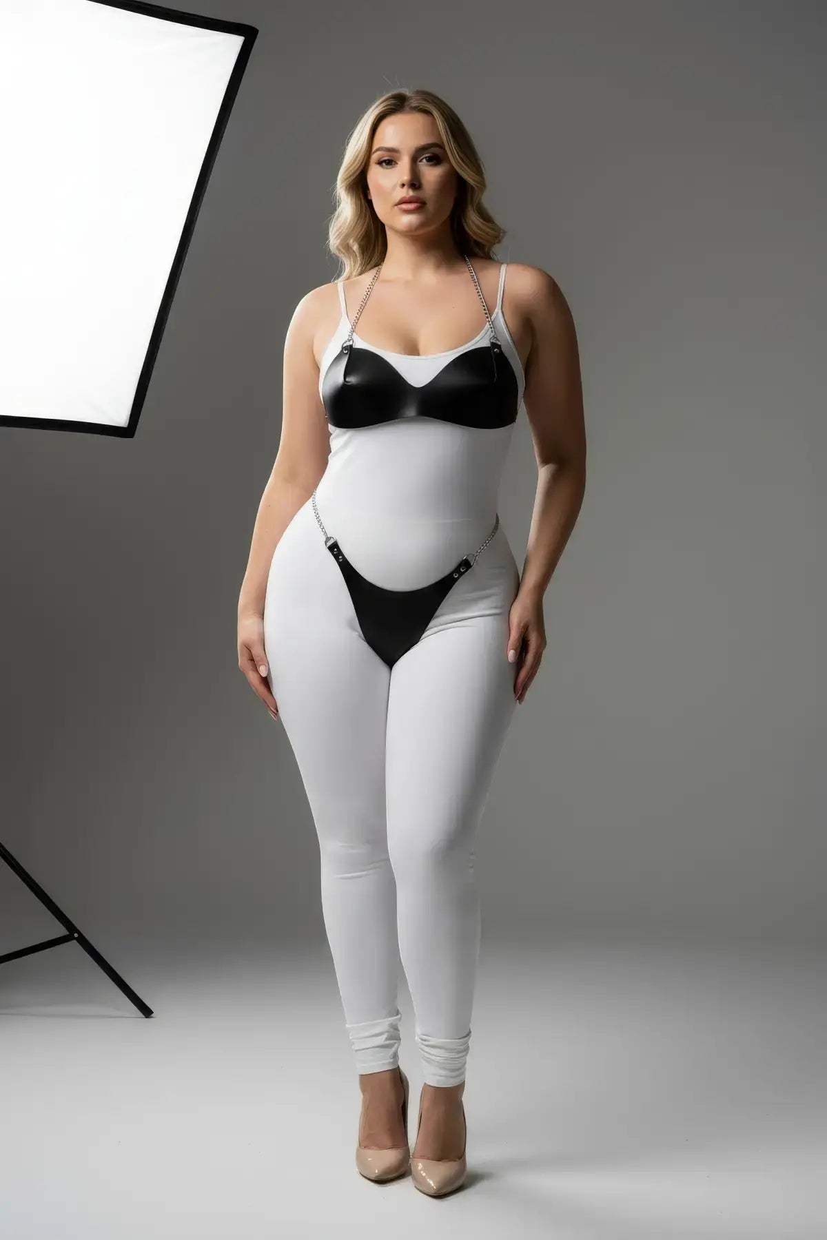 Plus-size harness set with black faux-leather cups and silver chain straps on a white bodysuit.