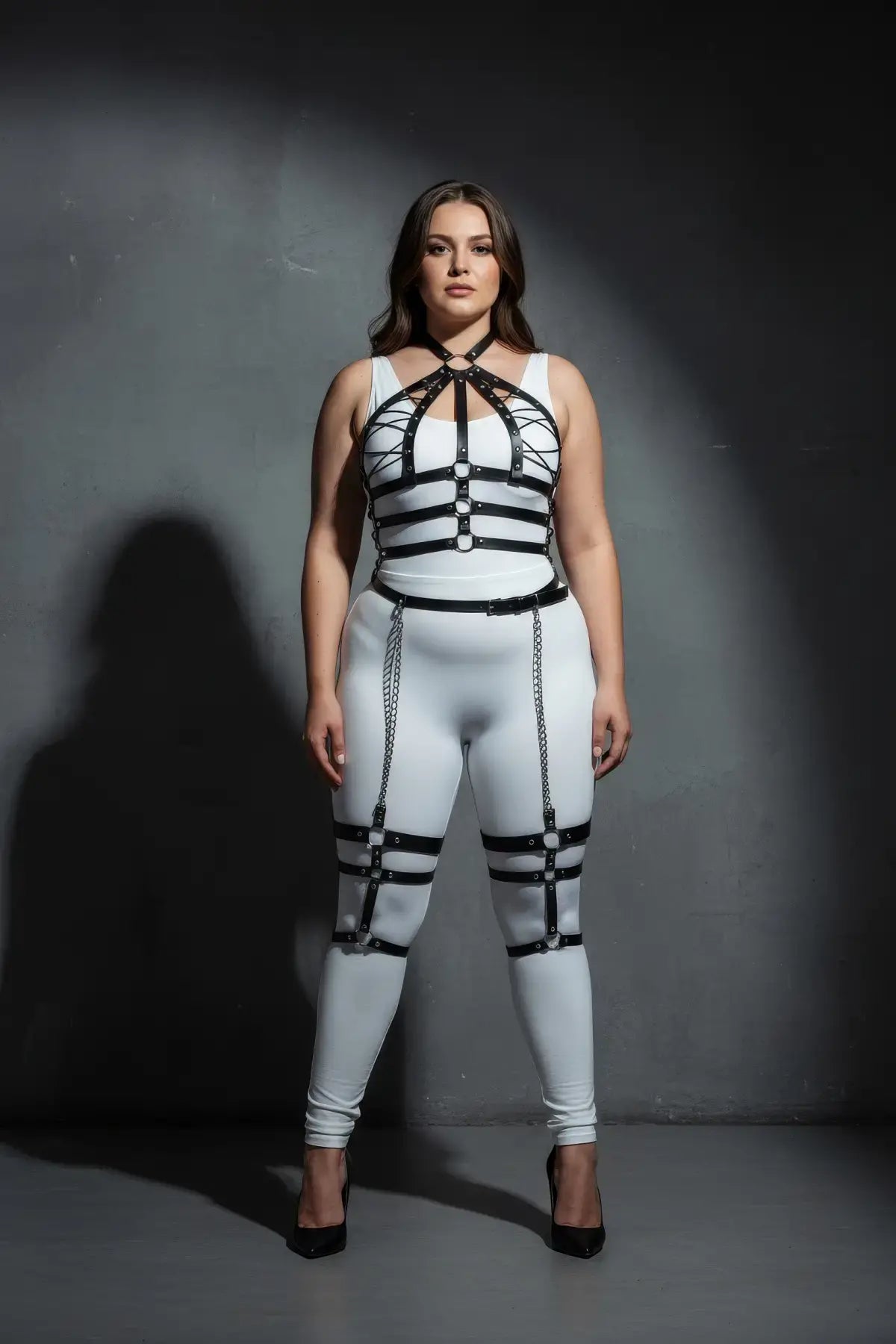 Plus-size black vegan-leather full-body harness with chain-draped lower half by HarnessClub over white bodysuit.