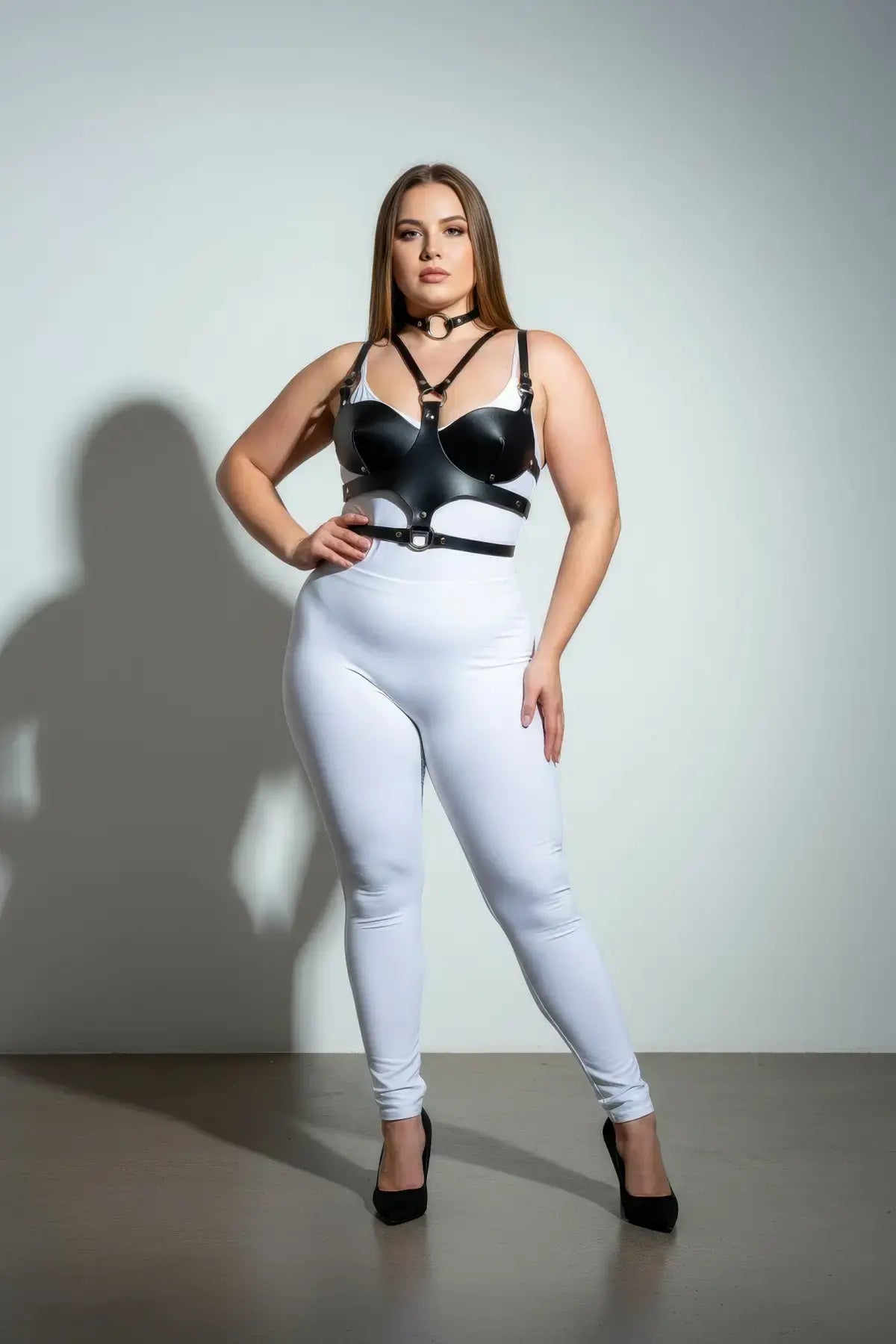 Plus-size black faux leather choker and chest harness set on model with white bodysuit and black heels