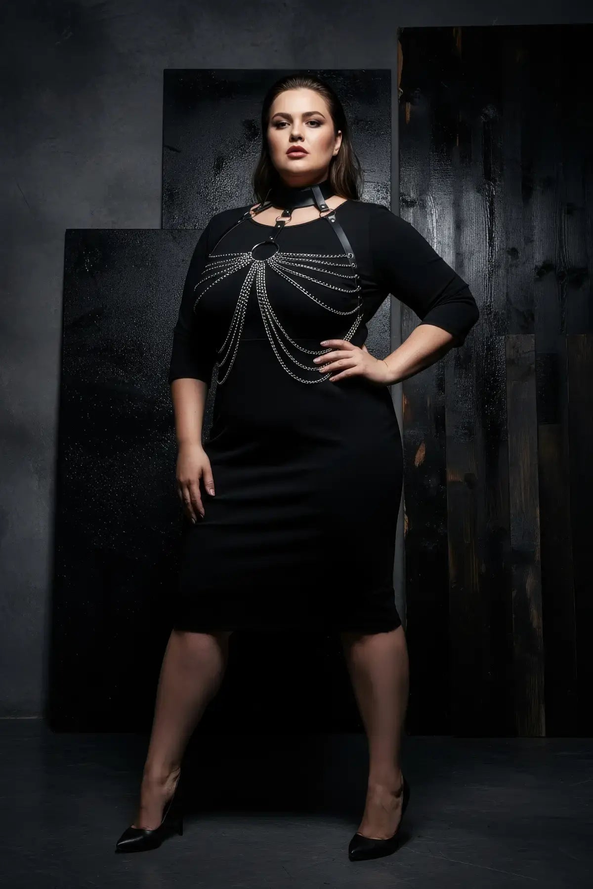 Plus-size black vegan-leather choker chain bib harness worn over a black dress