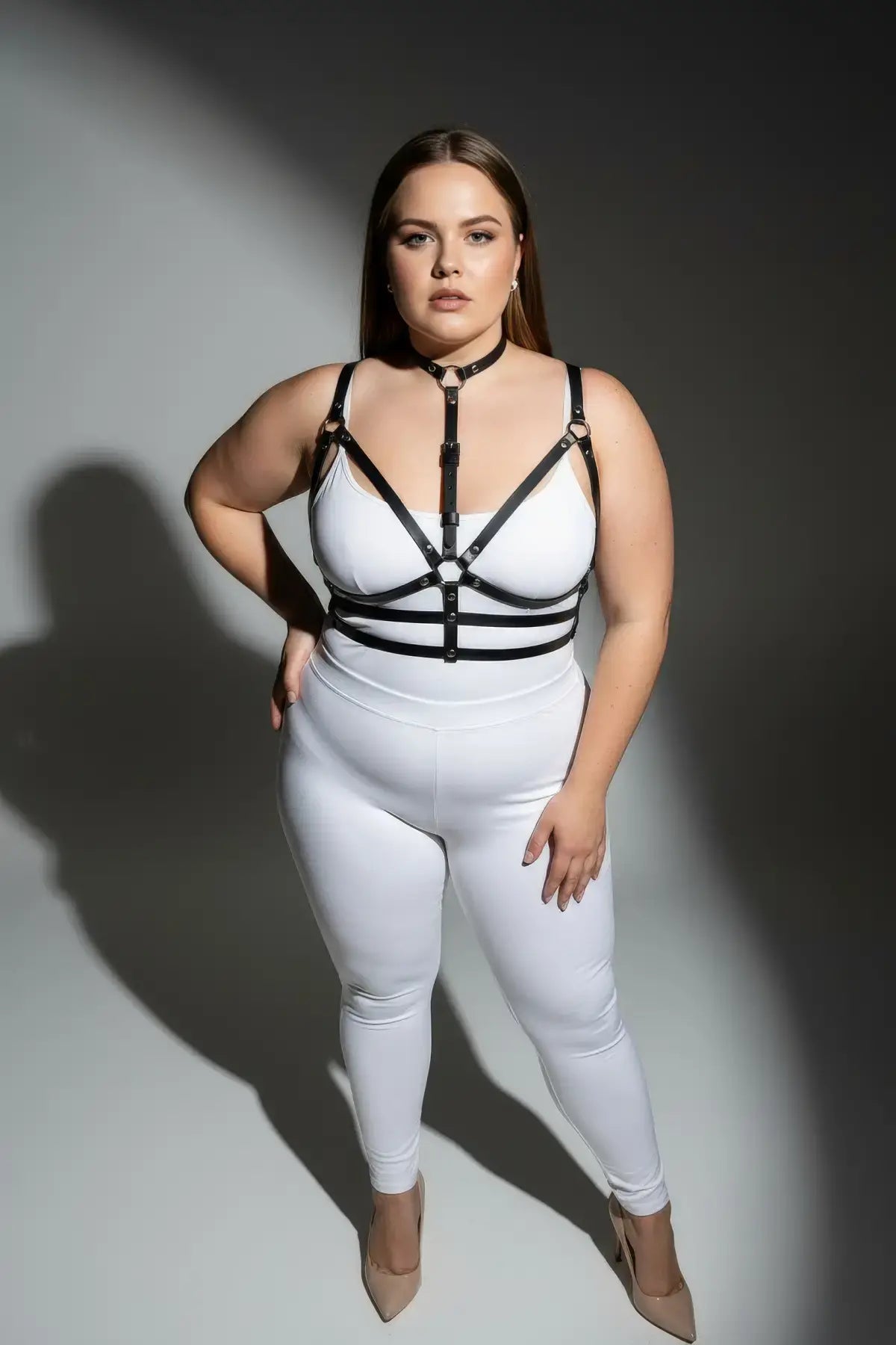 Plus-size black faux-leather harness set with collar and O-rings worn over a white bodysuit