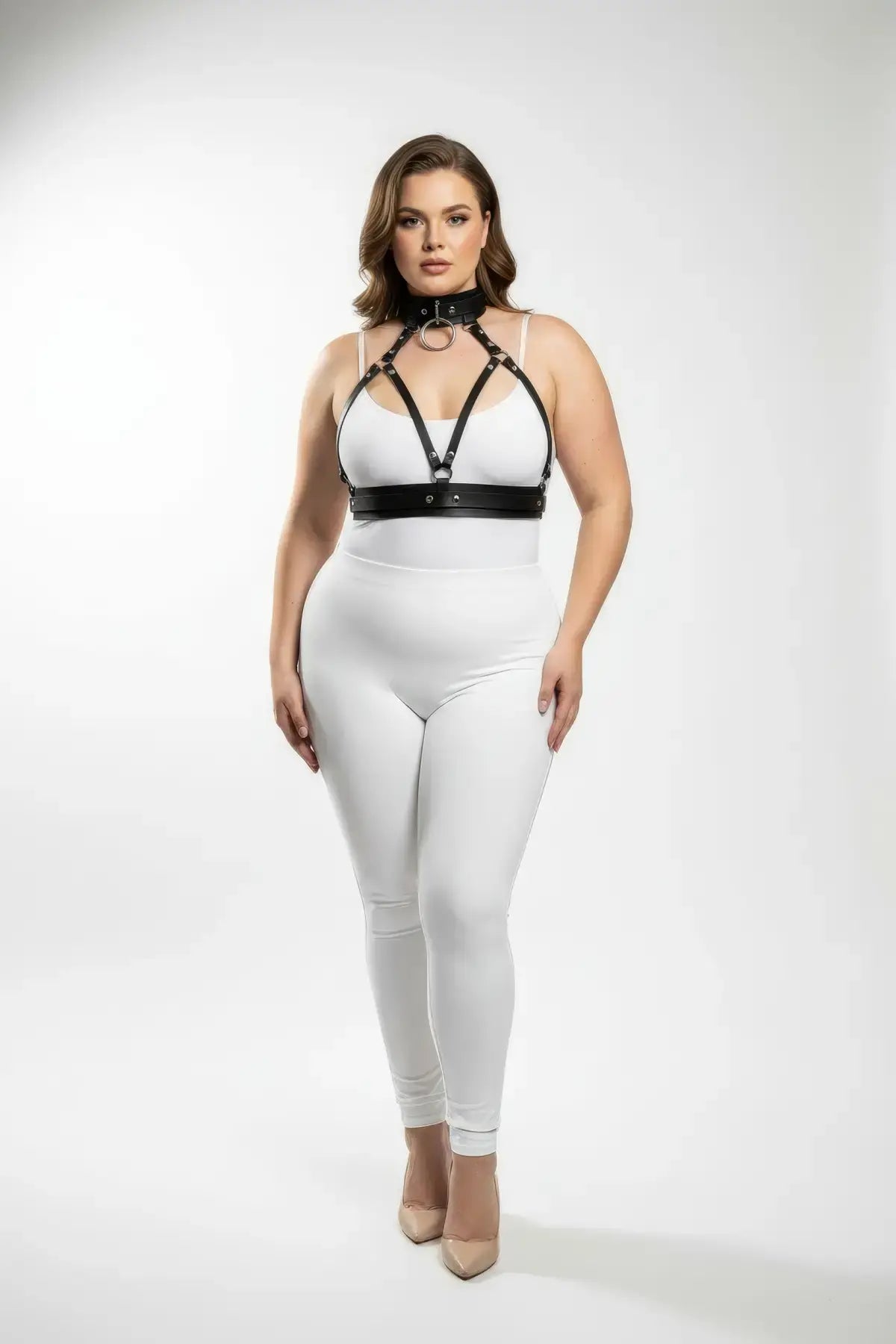 Plus-size black faux-leather harness set with collar, chest straps, and waist belt over white bodysuit