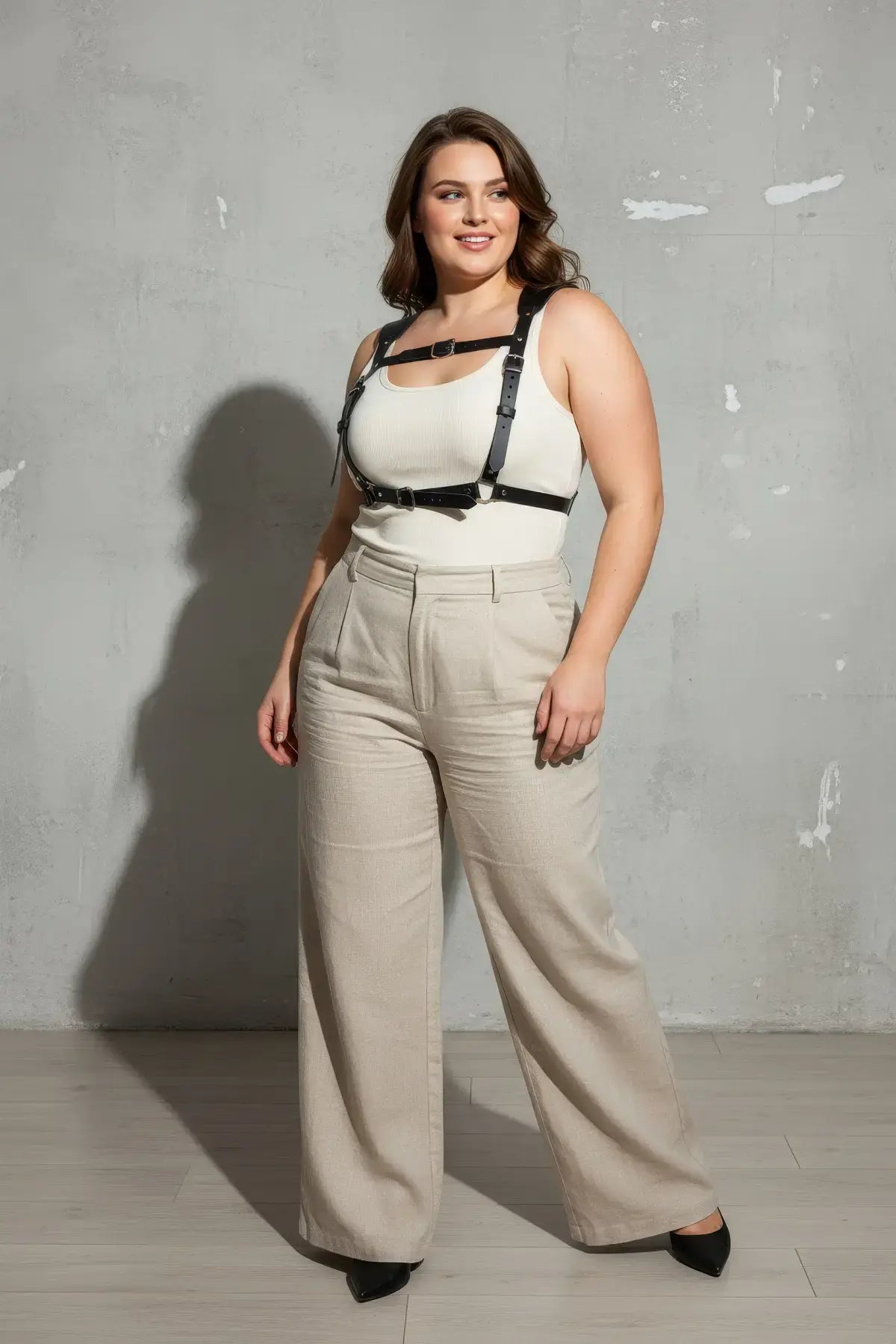 Plus size black corset-style leather body harness worn over a white tank top.
