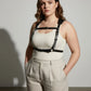 Plus-size black leather corset-style body harness by HarnessClub worn over a white ribbed tank top