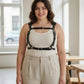 Plus size black corset-style leather body harness worn by a woman over a beige top, featuring shoulder and waist straps.