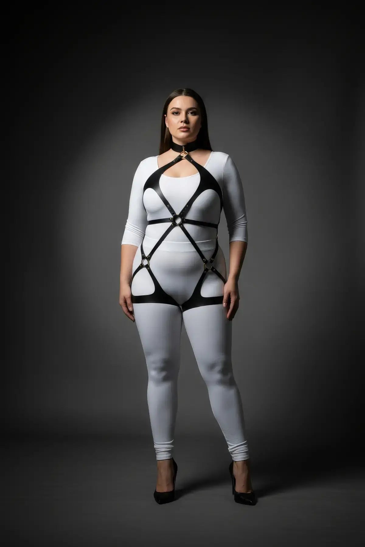 Plus-size black vegan-leather body harness with crisscross straps and choker collar, gold hardware over a white bodysuit.