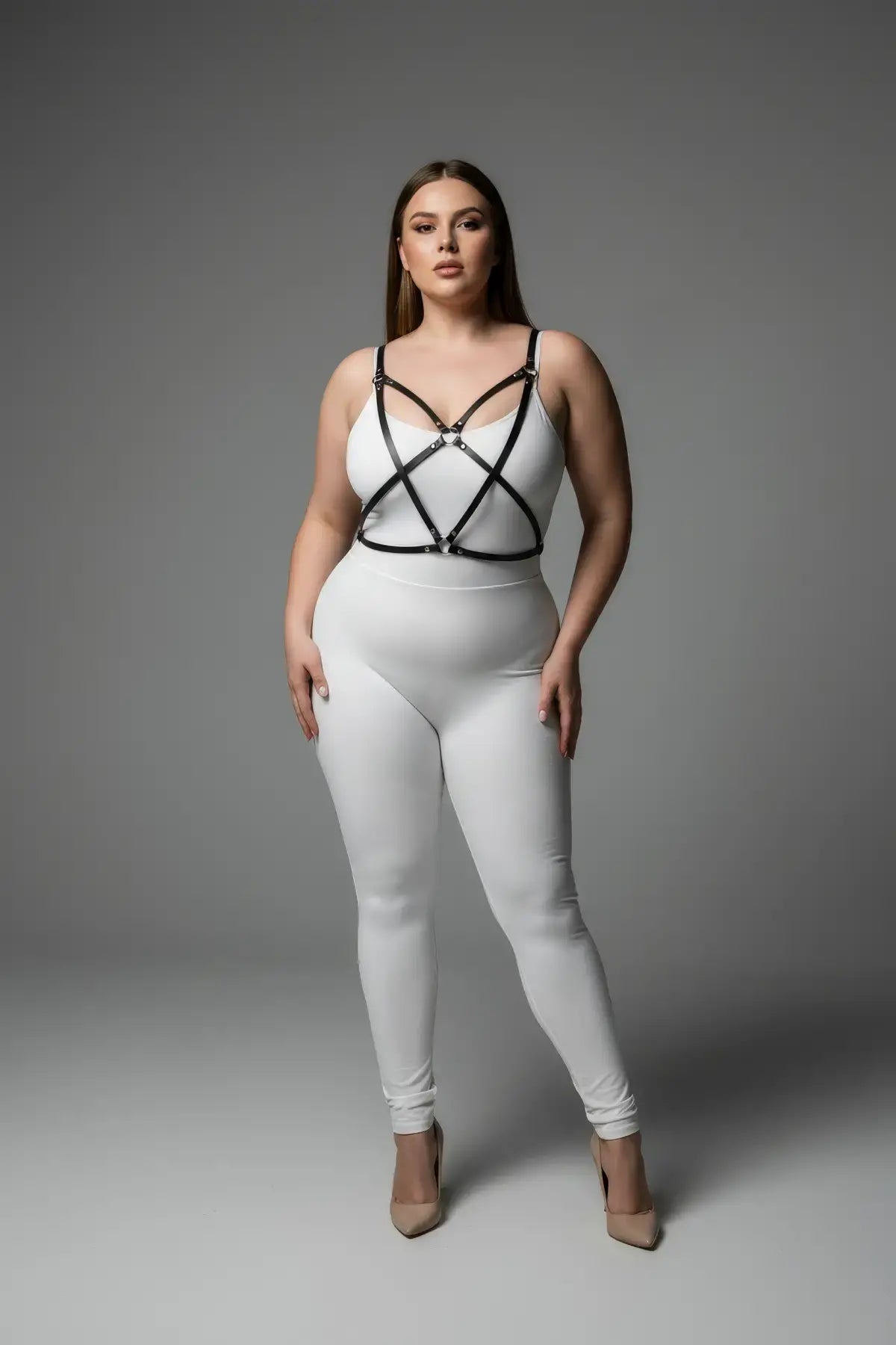 Plus-size black cross-strap faux leather harness worn over a white bodysuit.