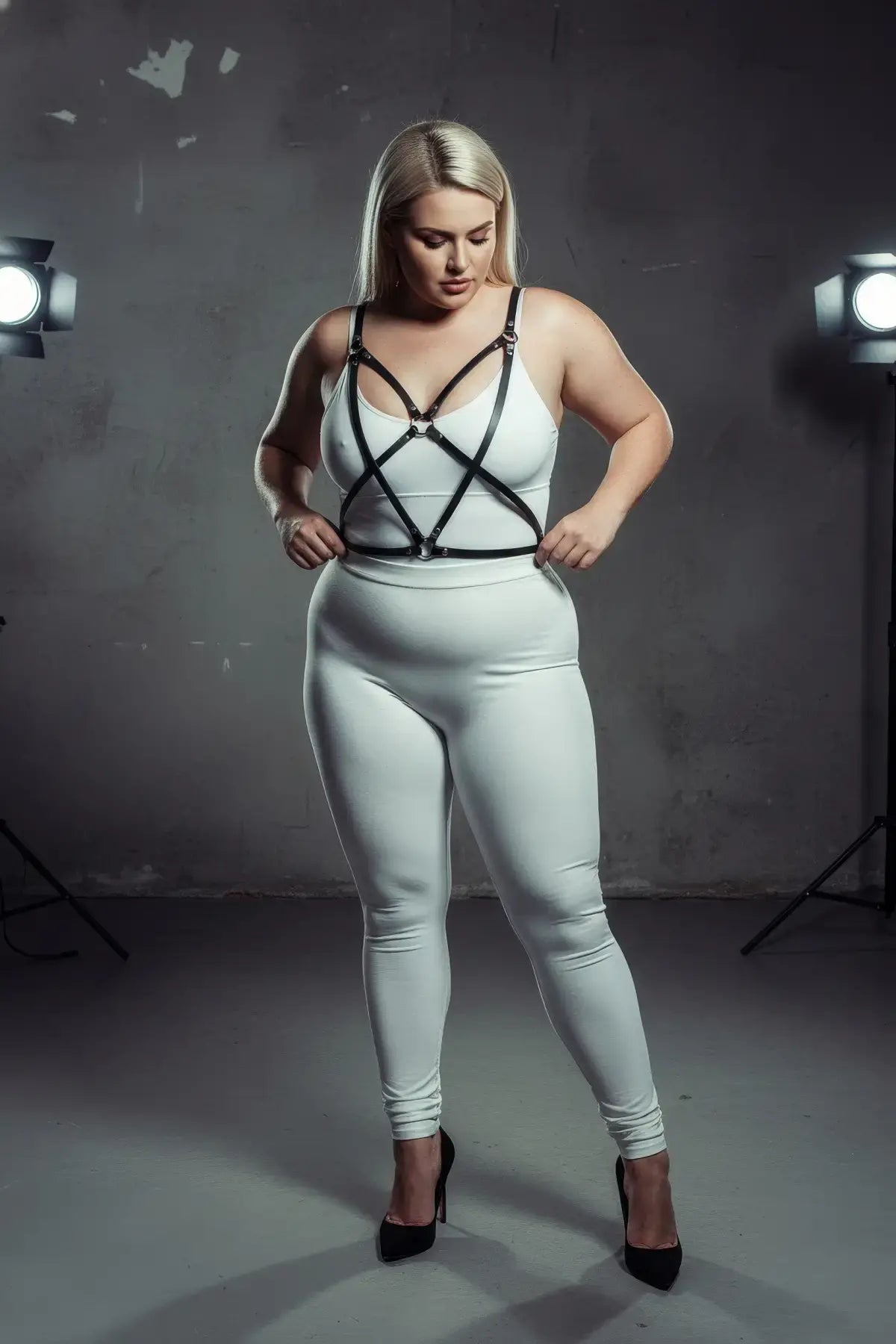 Plus-size black faux leather cross-strap harness worn over a white bodysuit