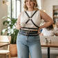 Plus-Size black leather cross-strap body harness by HarnessClub worn over a white sleeveless top