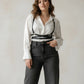 Plus-size black diagonal cross-strap vegan leather body harness worn over a white blouse, one-shoulder style.