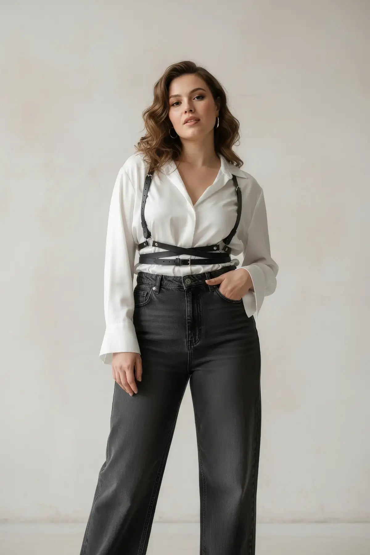 Plus-size black diagonal cross-strap vegan leather body harness worn over a white blouse, one-shoulder style.