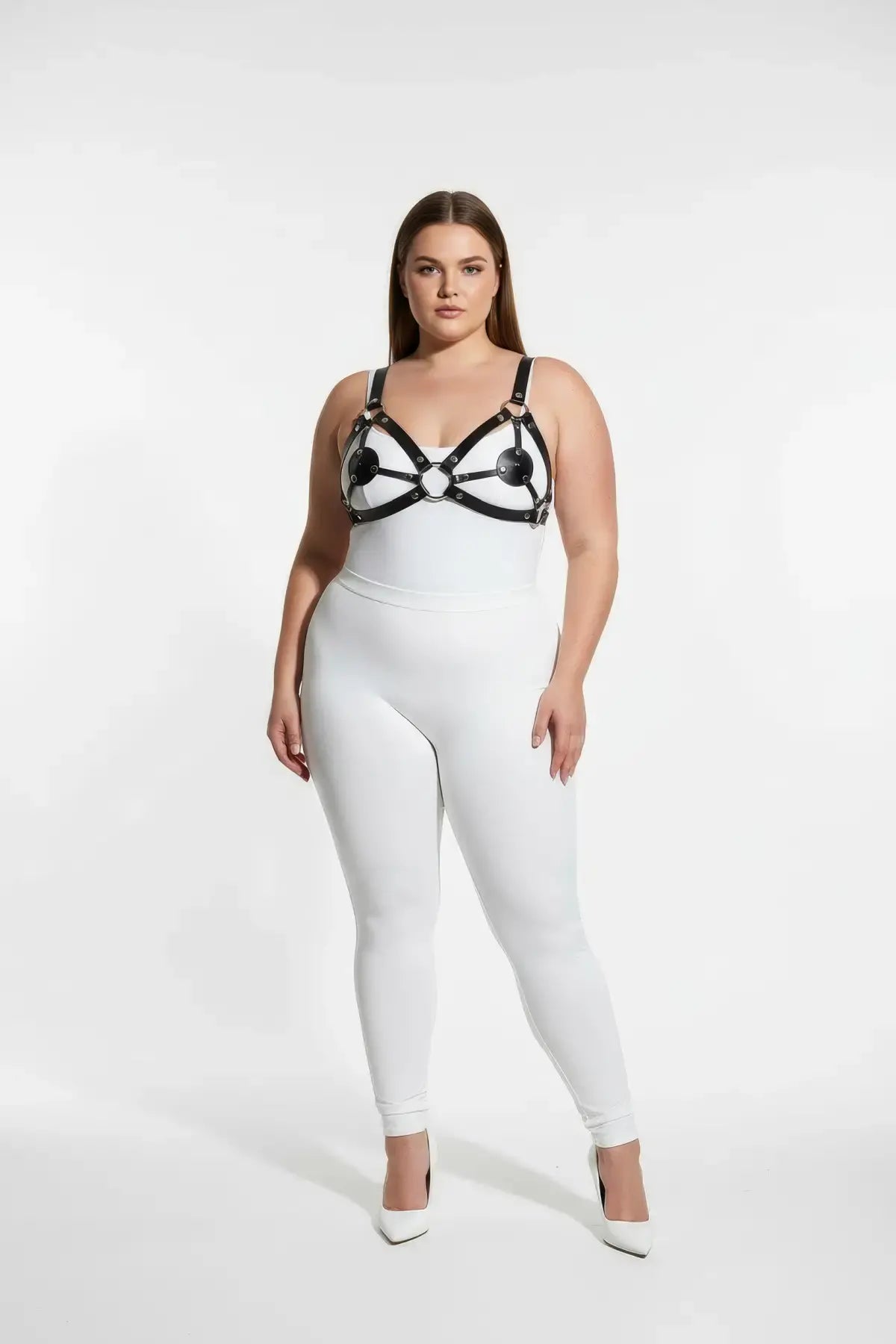 Plus-size black disc O-ring vegan leather chest harness worn over a white bodysuit.