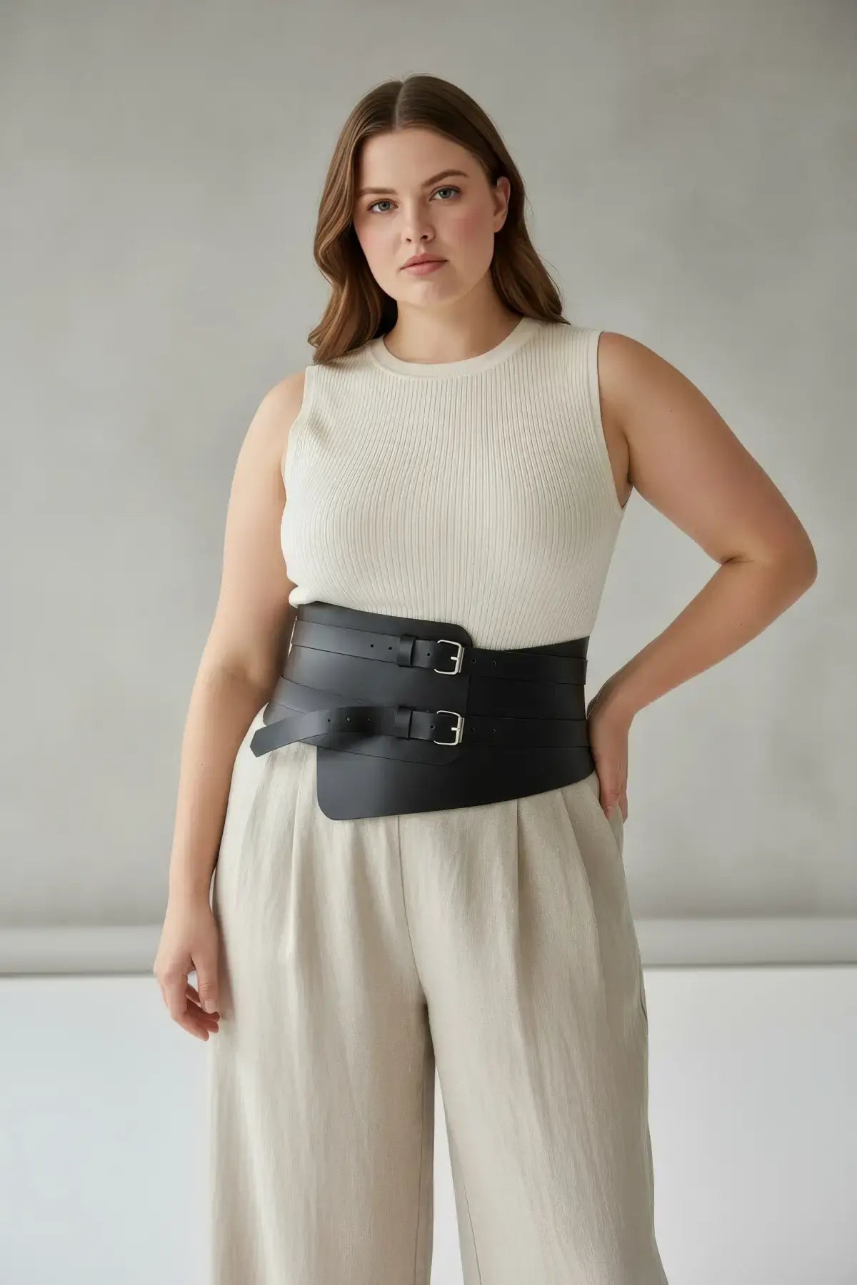 Plus-size black vegan leather waist cincher with two buckles worn over a sleeveless knit top