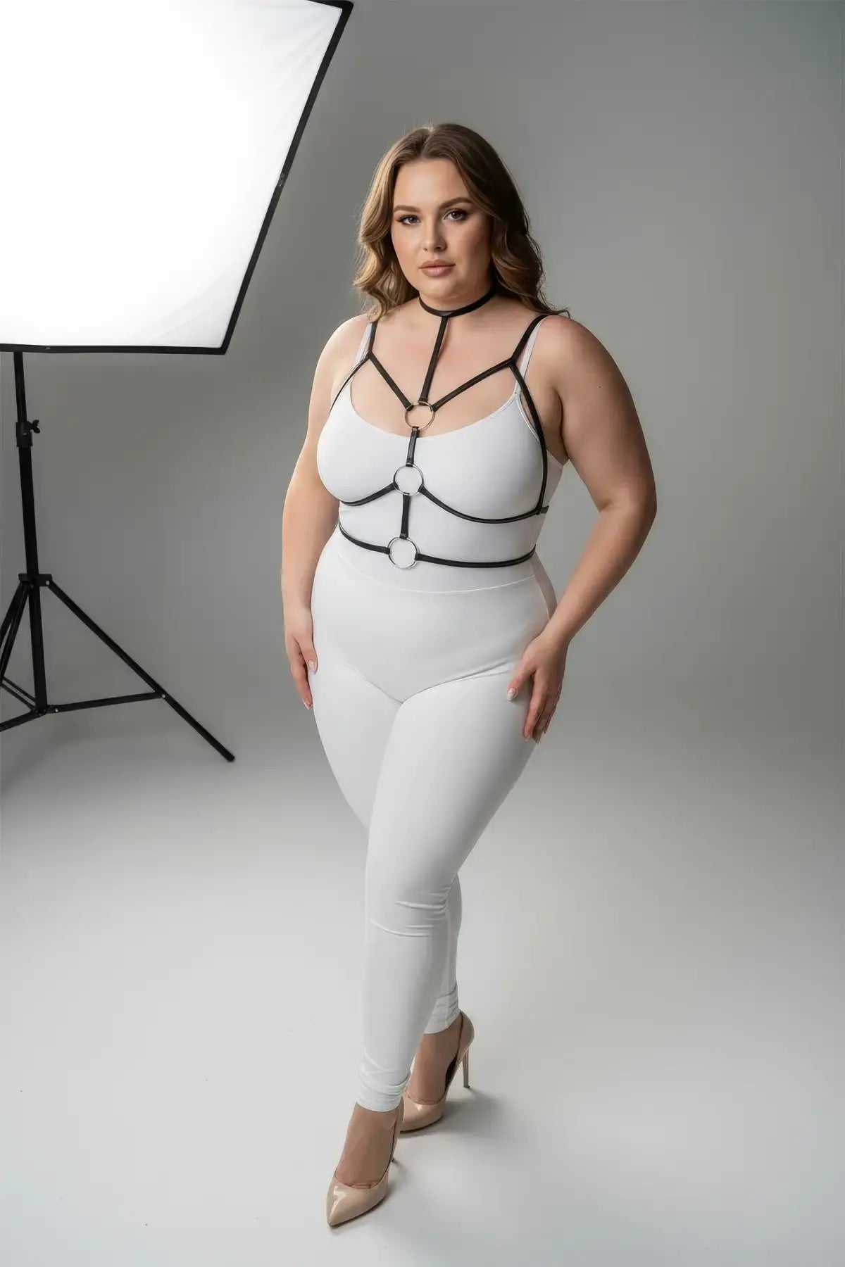 Plus size black elastic collar and O-ring harness with neck-to-waist straps worn over white bodysuit