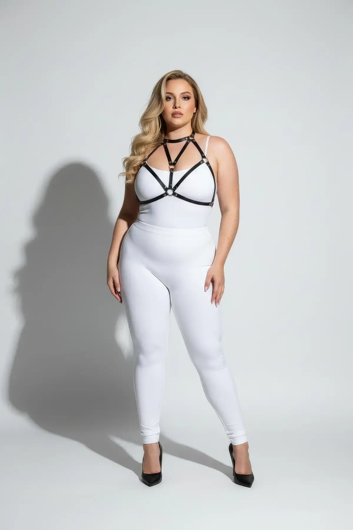 Plus size black faux leather chest harness by HarnessClub worn over a white bodysuit.
