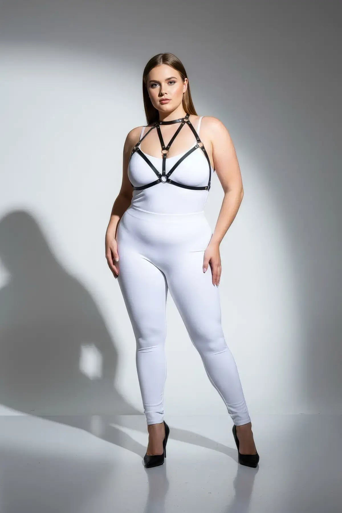Plus-size black faux leather chest harness by HarnessClub on a model in a white bodysuit.