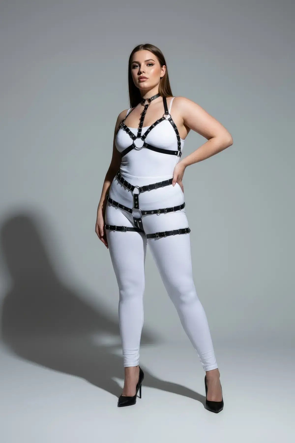 Plus-size black faux leather body harness by HarnessClub on white bodysuit, fully adjustable straps.