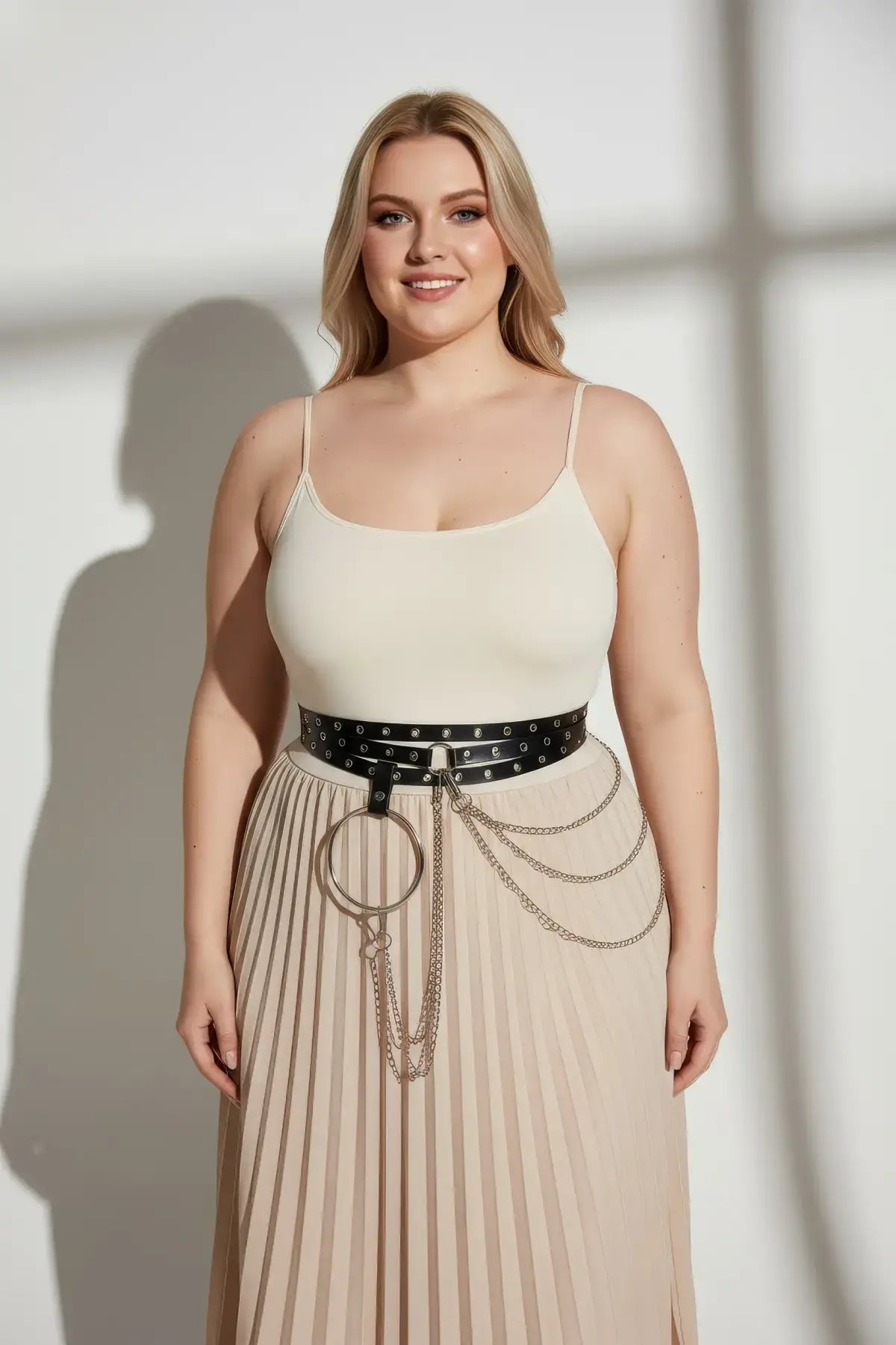 Plus-size black vegan-leather grommet belt with O-ring and chain detail at the waist over a cream top