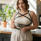 Plus-size black leather harness-style body accessory by HarnessClub worn over a beige ribbed tank top.