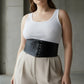 Plus size black lace-up corset belt by HarnessClub worn over white ribbed tank top.
