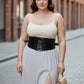 Plus size black lace-up corset waist belt worn over a white top and light gray dress on a city street.