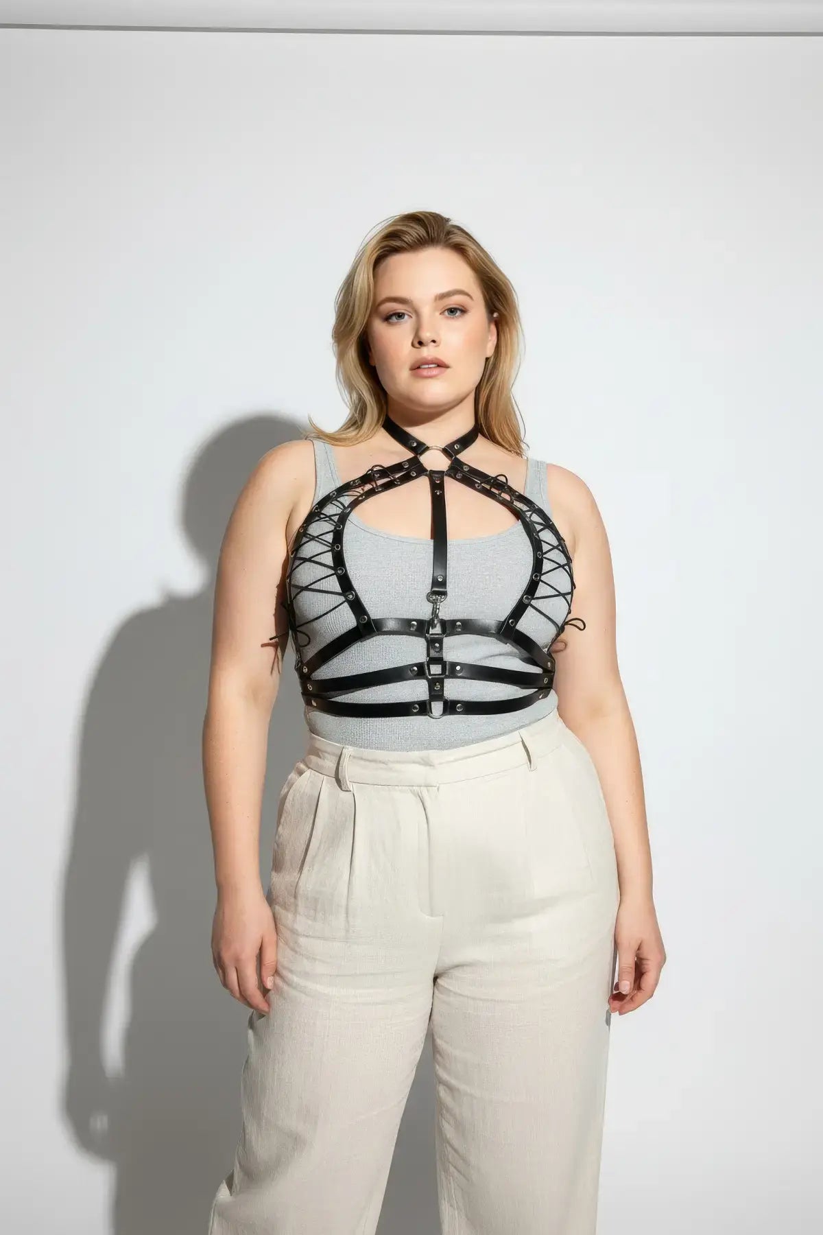 Plus-size black leather lace-up corset-style harness with strappy design worn over gray top by HarnessClub