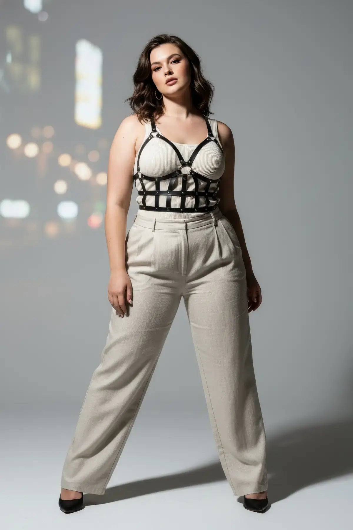 Plus size black leather body harness outfit completer worn over a white ribbed top and beige trousers