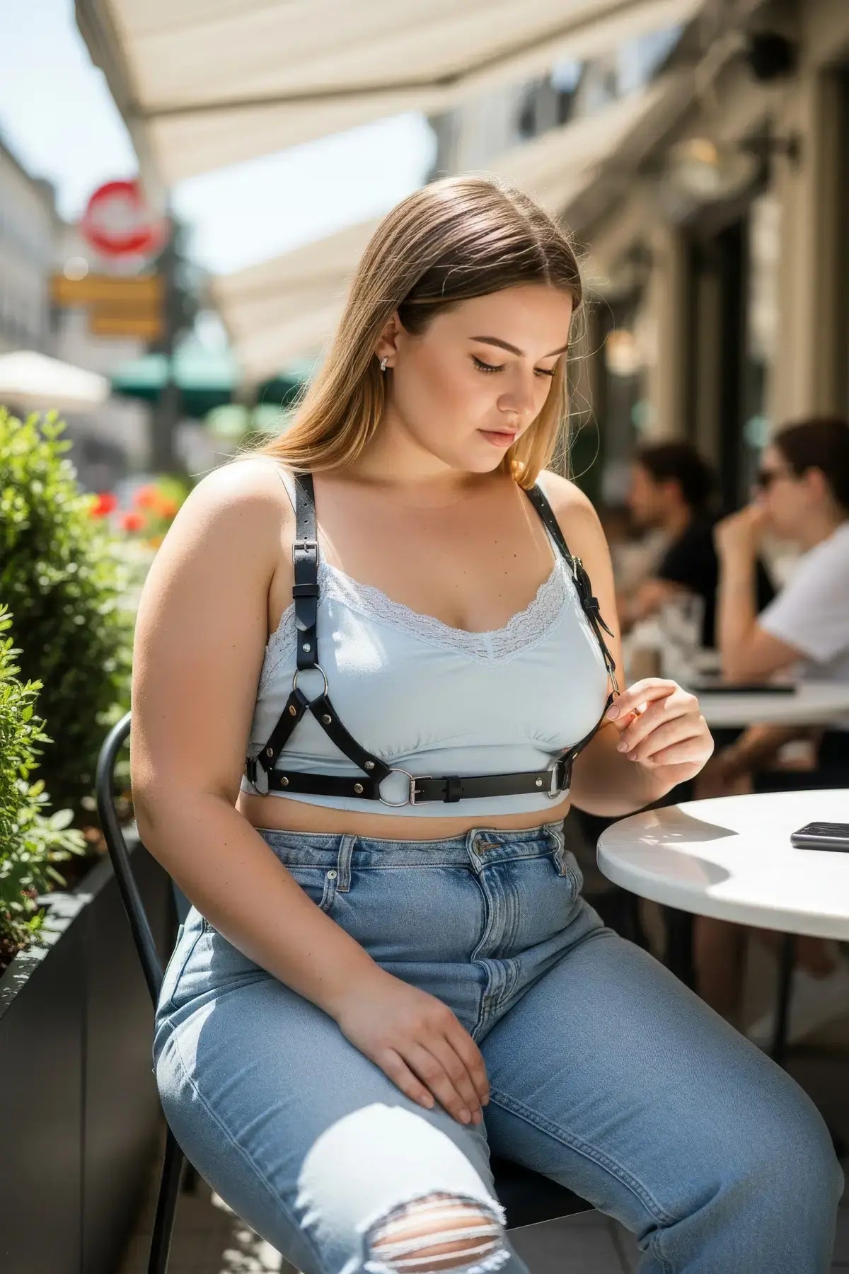 Plus size black leather harness body accessory with metal rings and buckles, worn over a light blue top.