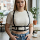 Plus Size black leather harness-look adjustable body accessory by HarnessClub worn over a cream knit top