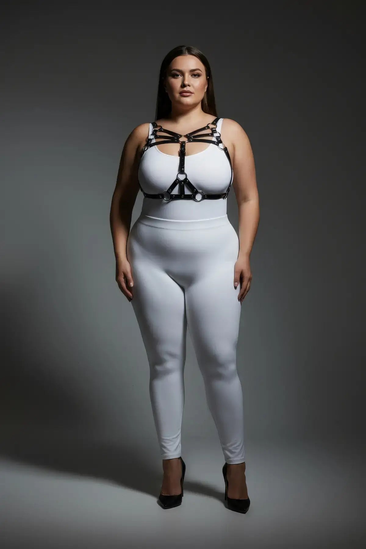 Plus-size black vegan-leather multi-band O-ring cage chest harness worn over a white bodysuit