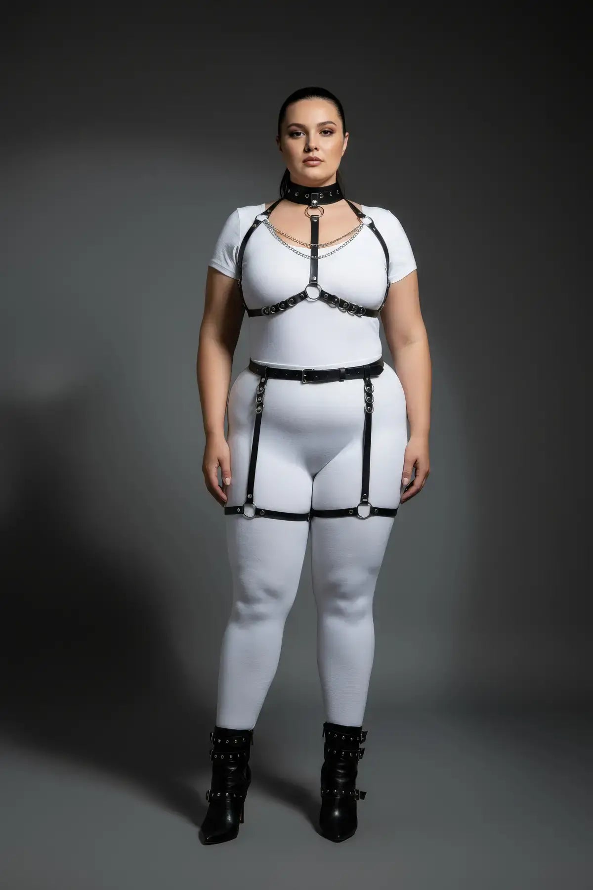Plus-size black vegan leather full-body harness with O-ring chains and garter straps on model.