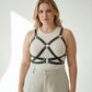 Plus-size black leather harness with O-ring hardware worn over a beige ribbed top