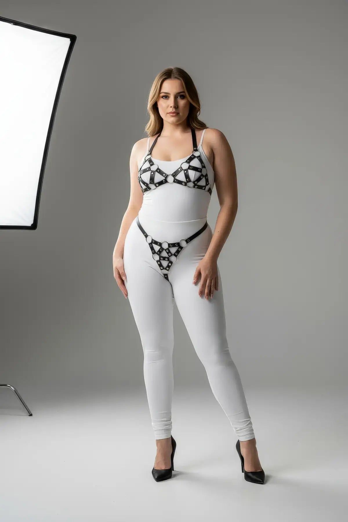 Plus-size black faux-leather O-ring body harness set by HarnessClub, worn over a white bodysuit