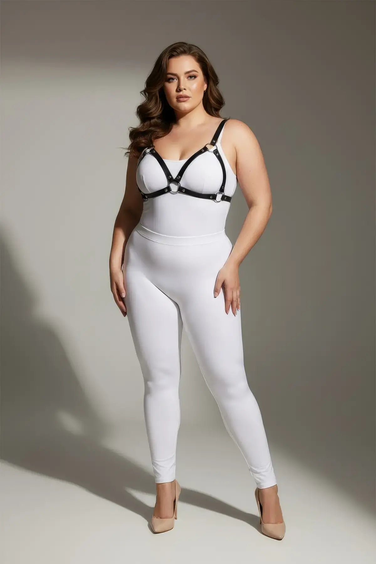 Plus-size black faux-leather O-ring bra harness by HarnessClub worn over a white bodysuit.
