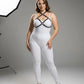 Plus-size black faux-leather O-ring chest harness with metal hardware, worn over a white bodysuit and beige heels.
